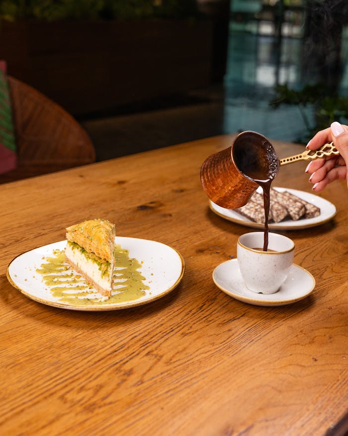 A cup of coffee being poured with desserts on a wooden table, creating a warm, inviting atmosphere.