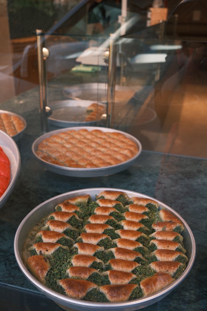 Round trays of freshly baked baklava with pistachio filling displayed in a bakery window.