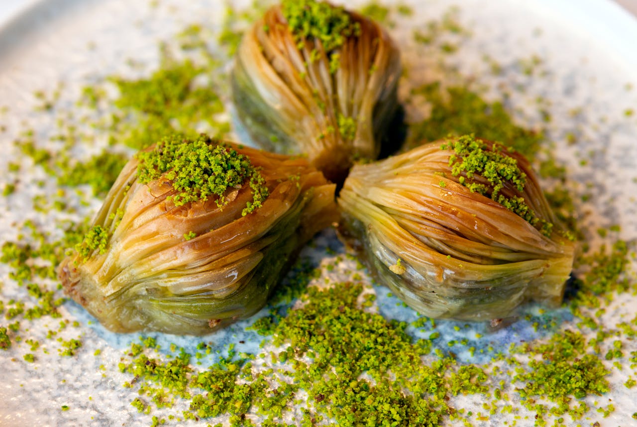 Close-up of three Turkish baklava topped with ground pistachios on a plate.