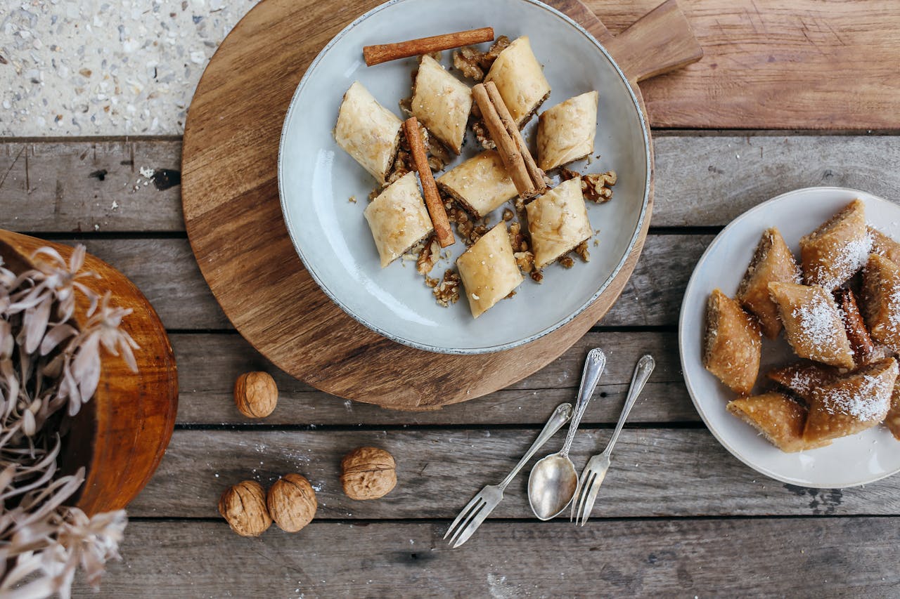 Sliced baklava on plates with cinnamon sticks and walnuts on a rustic wooden table.