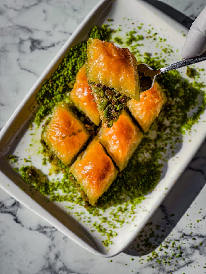 Close-up of golden baklava slices with pistachio on a marble background, presented on a white plate.